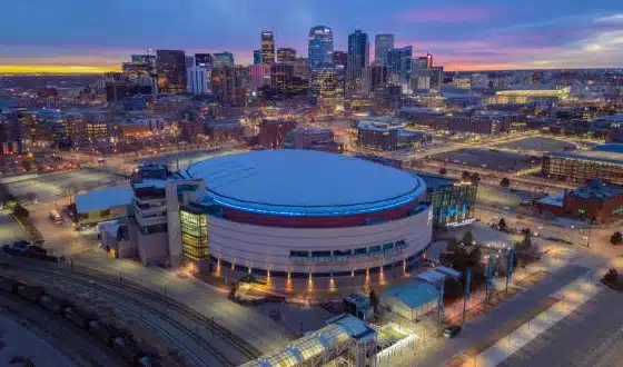 Aerial view of Ball Arena Denver at night with the downtown Denver skyline glowing in the background at sunset