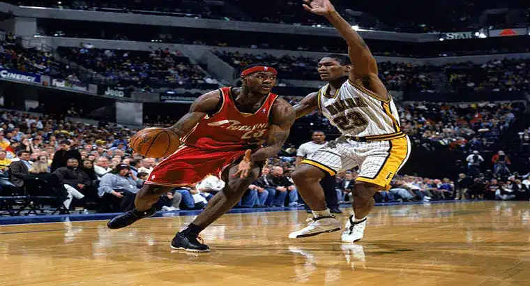 Young LeBron James in Cleveland Cavaliers red jersey driving to the basket against an Indiana Pacers defender during a 2003 NBA regular season game at Conseco Fieldhouse